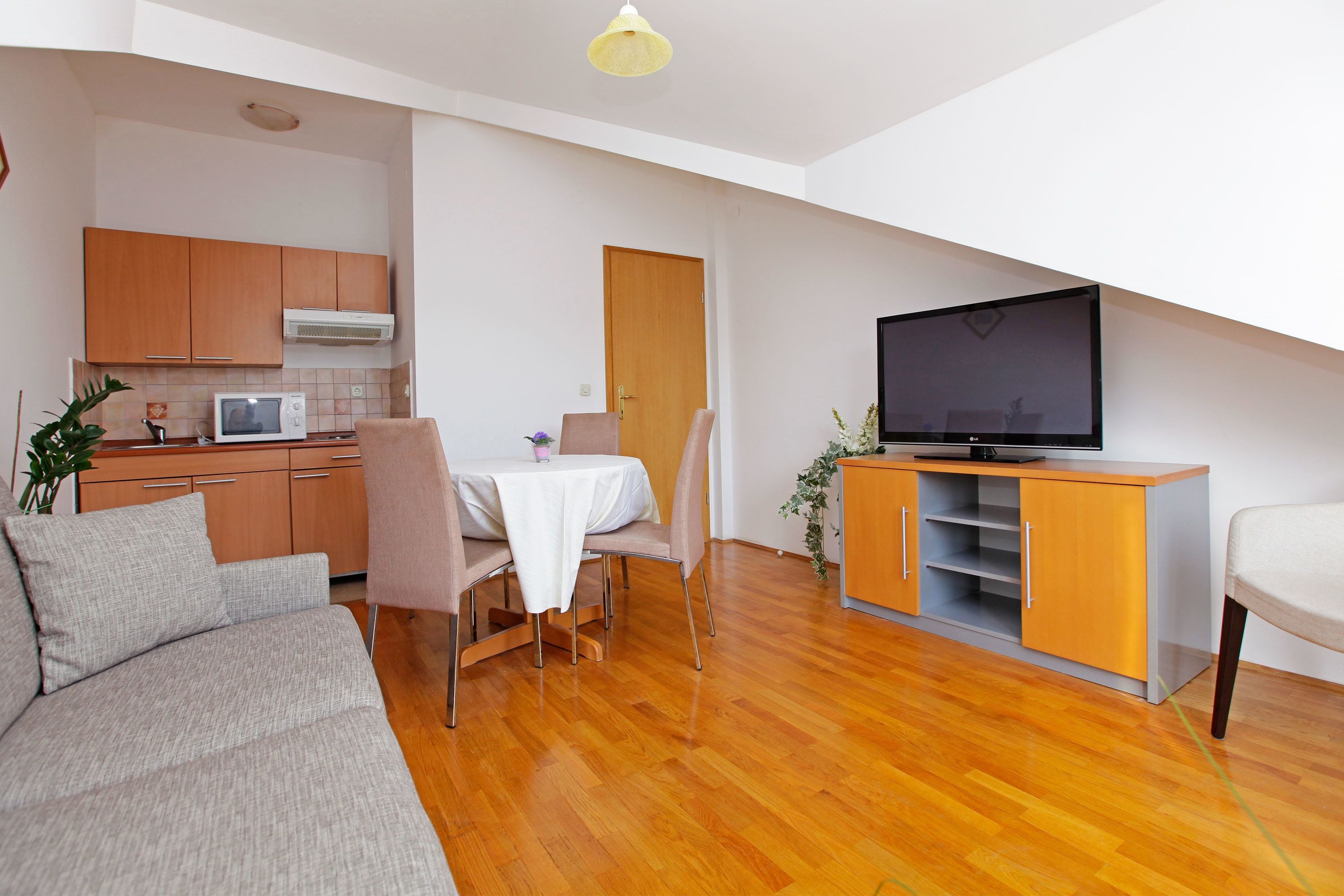A modern living room with a sofa, dining table, chairs, a TV, and a kitchen area with cabinets and appliances.