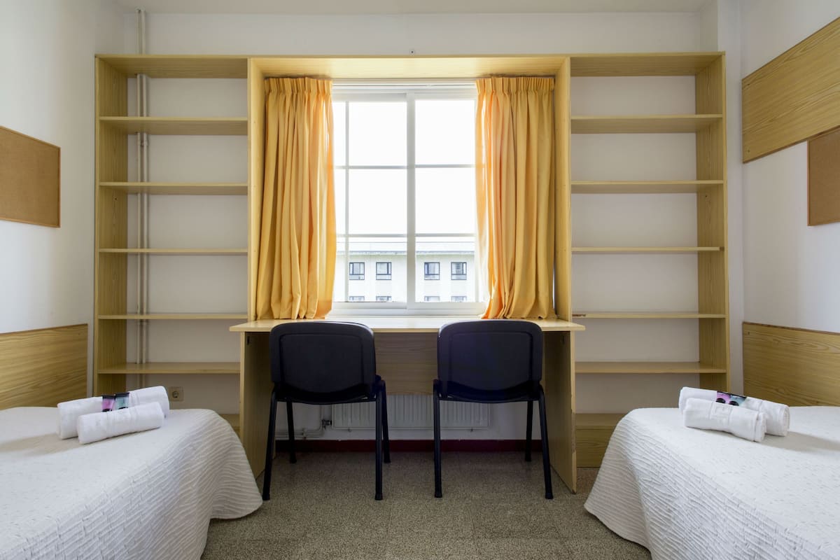 Une chambre d’hôtel avec deux lits, un bureau et une fenêtre avec des rideaux.