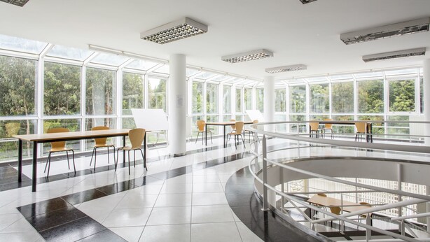 Un vaste espace intérieur doté de grandes fenêtres, de nombreuses tables et chaises, et d’un escalier central.
