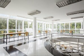 A spacious indoor area with large windows, multiple tables and chairs, and a central staircase. - Residencia Universitaria Resa Siglo XXI (Culleredo)