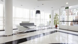 Un hall d’entrée moderne avec un sol à carreaux, des meubles blancs et de grandes fenêtres.