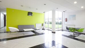 Un hall d’entrée moderne avec un mur vert vif, un canapé gris, des fauteuils à bascule blancs et une table avec des chaises vertes.
