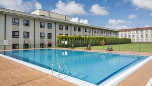 Une piscine avec une terrasse carrelée, un poste de surveillance pour le sauveteur et une haie.