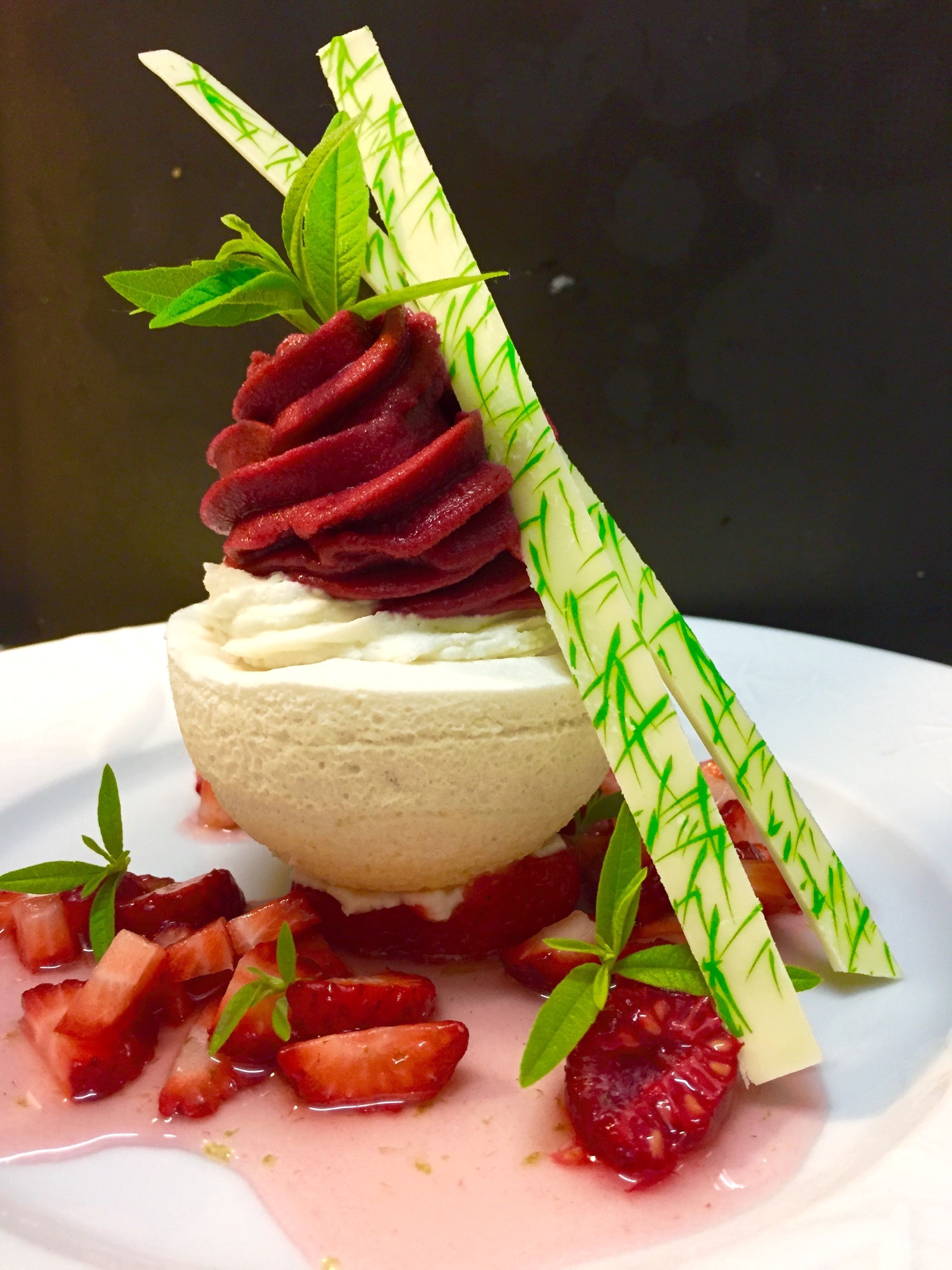 A dessert with a creamy base, topped with a red swirl, surrounded by strawberries and green leaves.