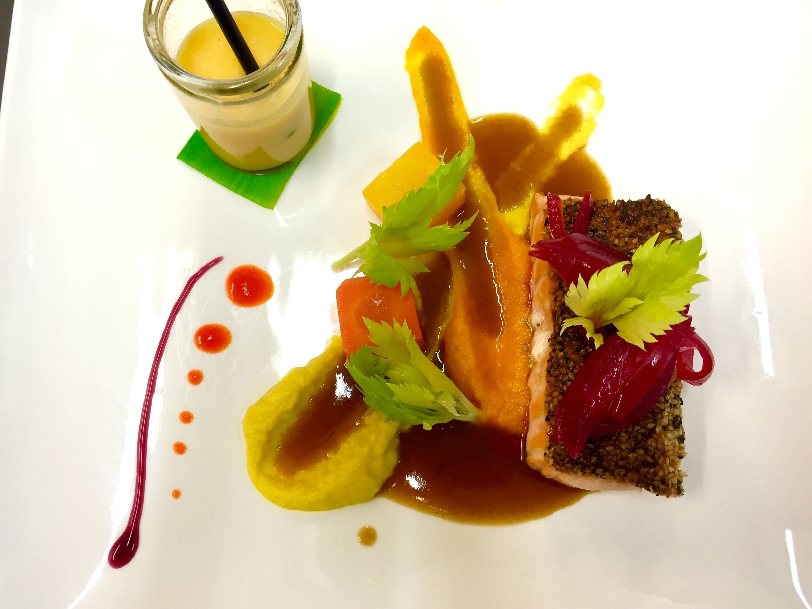 Une assiette à dessert contenant divers aliments, notamment une part de gâteau, une tranche de fruit et une sauce, accompagnée d’un verre d’une boisson jaune.