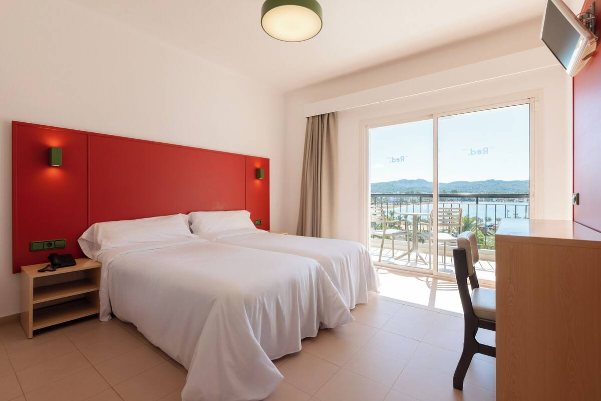 Ein Hotelzimmer mit zwei Betten, einem Schreibtisch und einem Balkon mit Meerblick.