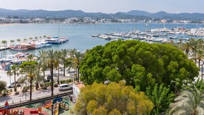 Un puerto costero con barcos, un parque infantil y vistas de la ciudad y montañas a lo lejos.