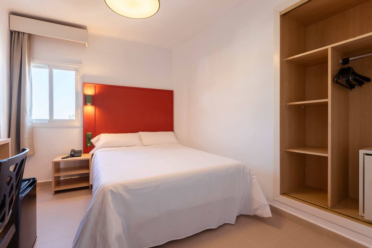 Ein Hotelzimmer mit Bett, Nachttisch, Kleiderschrank und Stuhl.