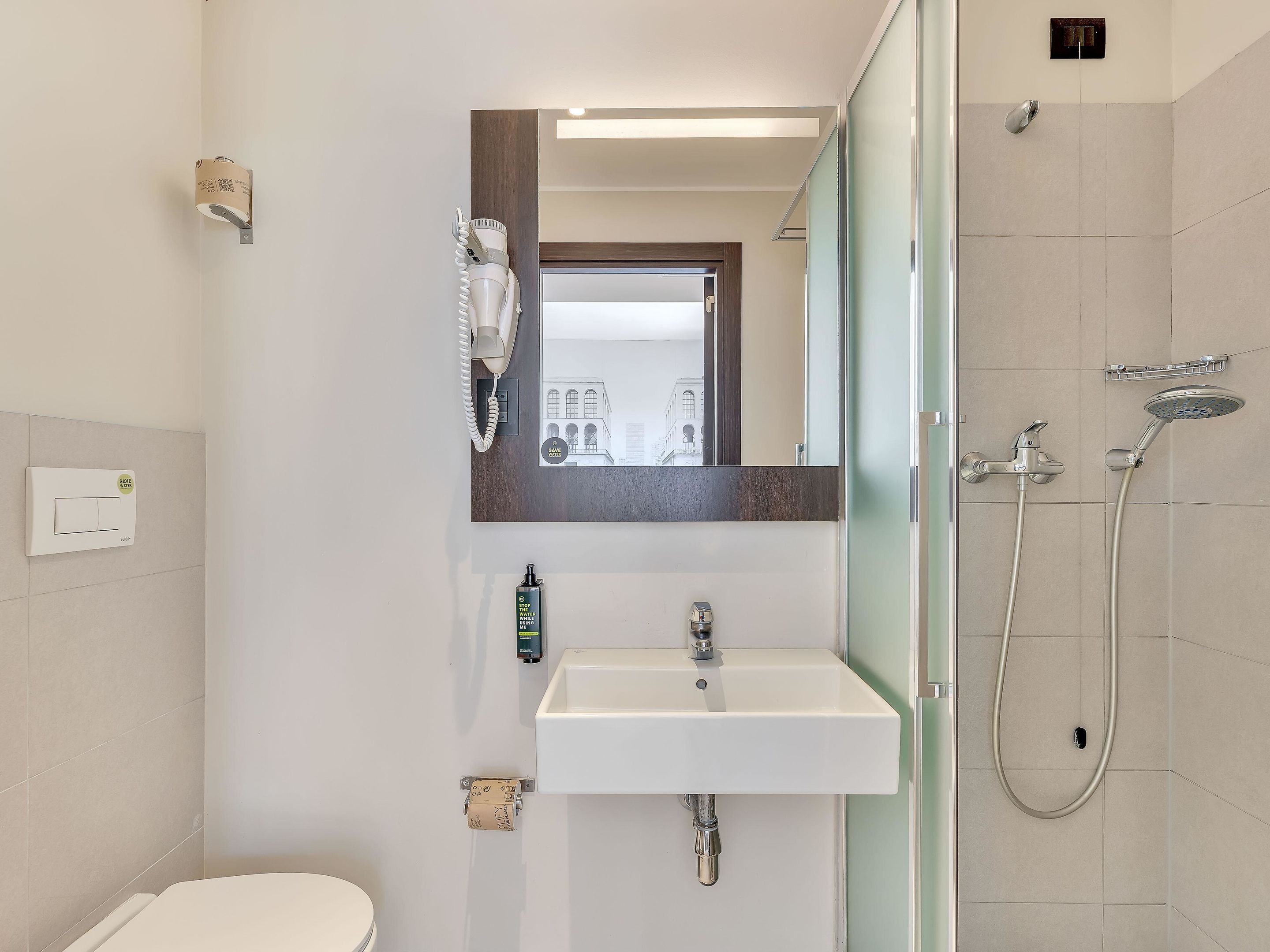 Et moderne badeværelse med toilet, vask, spejl og brusebad.