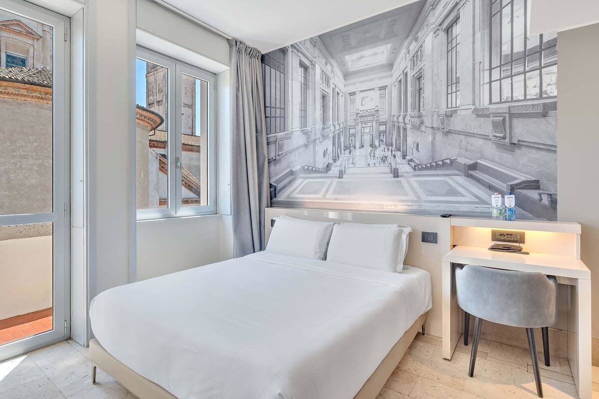 A hotel room with a large bed, a desk with a chair, and a mural of a city street.