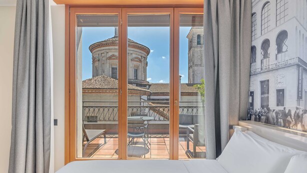 A hotel room with a large bed, a balcony with a table and chairs, and a view of a historic building with a dome and arches. - B&B Hotel Milano Sant'Ambrogio (Milan)
