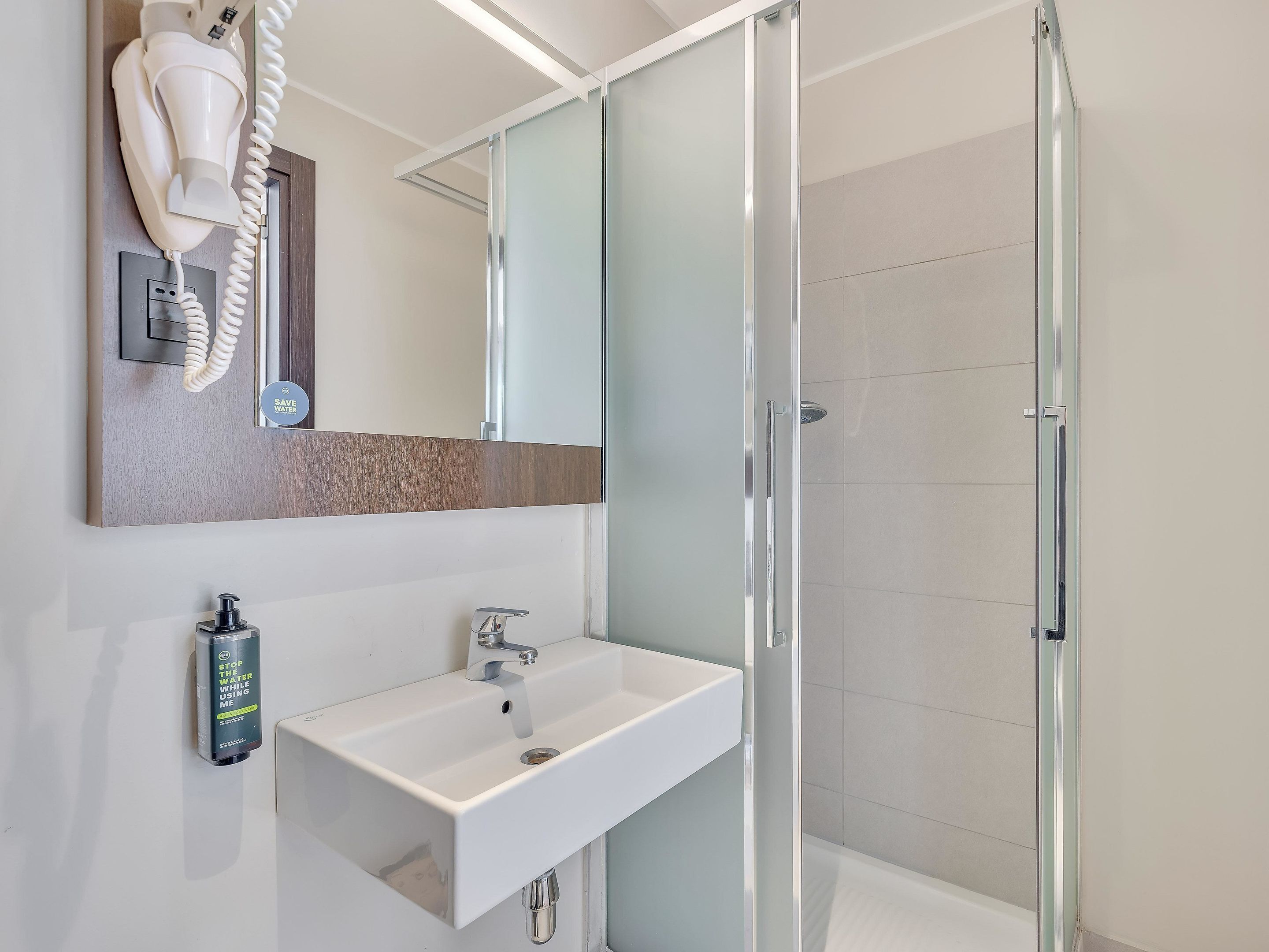 A modern bathroom with a glass shower enclosure, a white sink, and a hairdryer mounted on the wall.
