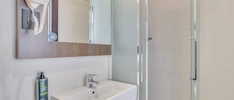 Une salle de bain moderne avec une douche à parois de verre, un lavabo blanc et un sèche-cheveux fixé au mur.