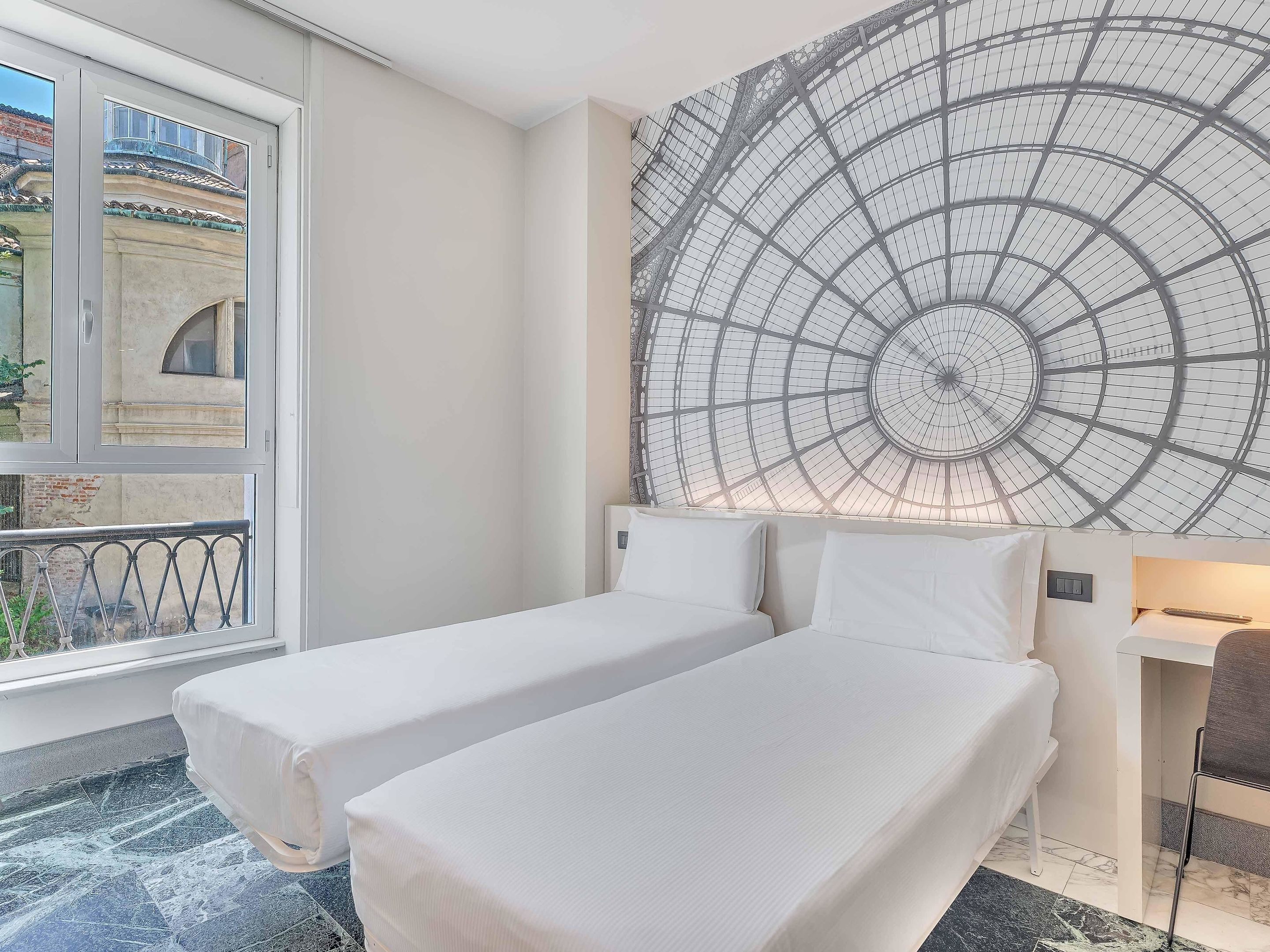 Ein Hotelzimmer mit zwei Einzelbetten, einem großen Fenster und einem außergewöhnlichen Deckenstil.