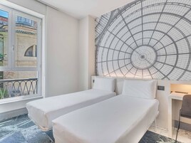 Una camera d'albergo con due letti singoli, un'ampia finestra e un design di soffitto originale.