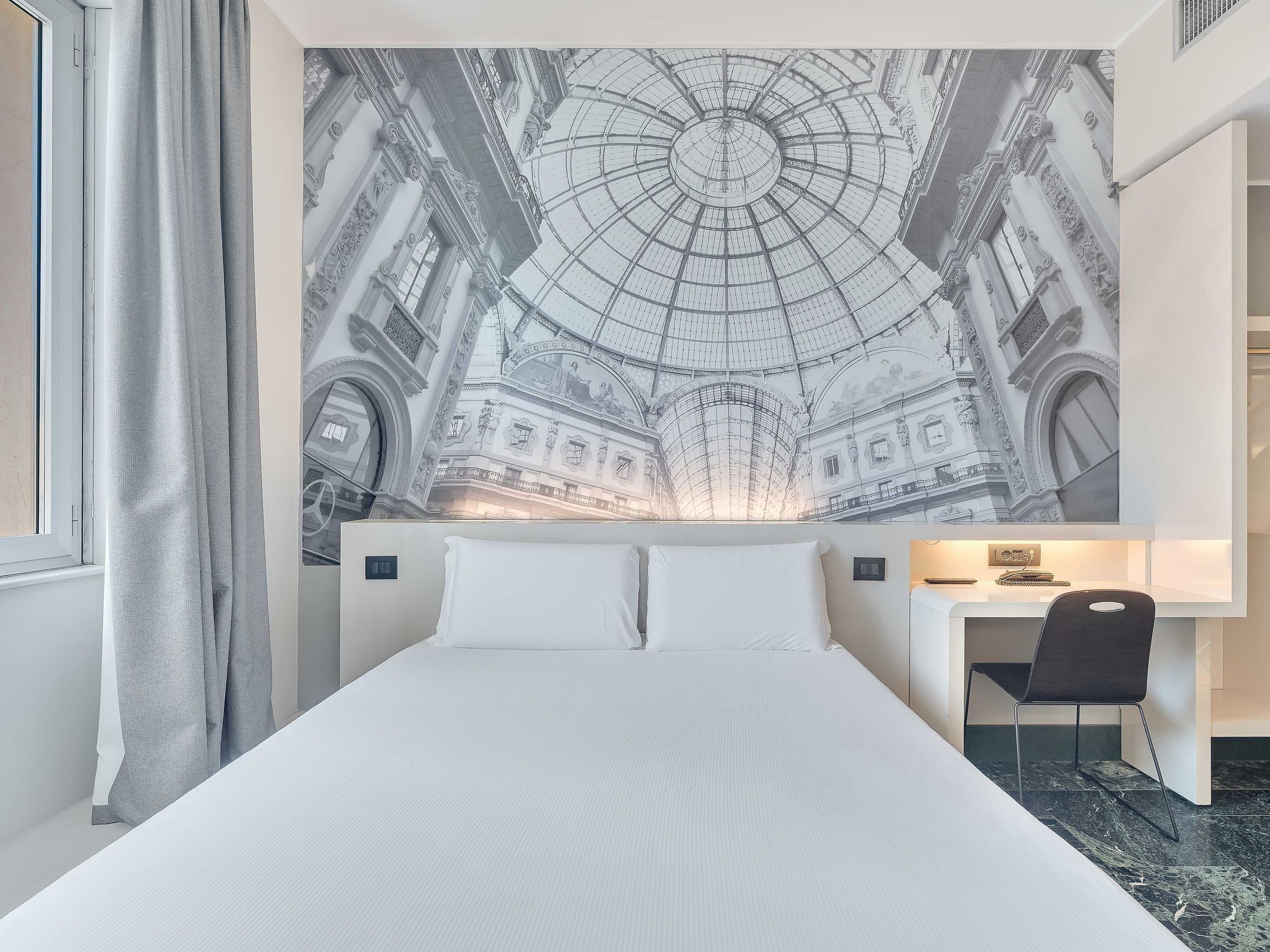 A hotel room with a large bed, a desk, and a wall mural of a historical building.