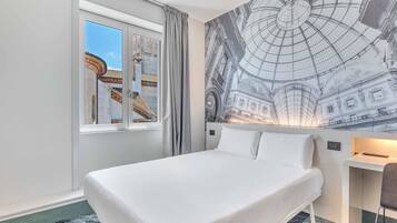 A hotel room with a large bed, a window with a view of a building, and a mural of a historical building on the wall.