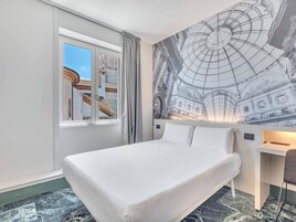 Camera d'albergo con un letto grande, una finestra vista su un edificio e un murale raffigurante un edificio storico.