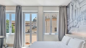 A hotel room with a large bed, a view of the cityscape through the windows, and a mural on the wall. - B&B Hotel Milano Sant'Ambrogio (Milan)