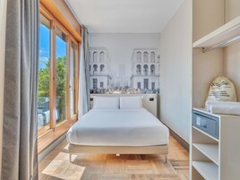 Una camera d'albergo con un letto grande, vista sulla città dalla finestra e un comodino con una lampada.