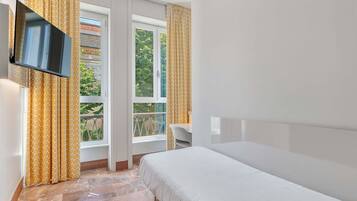 Habitació d'hotel amb llit, televisió penjada a la paret i finestra amb cortines.