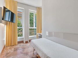 Una habitación de hotel con una cama, un televisor montado en la pared y un ventanal con cortinas.