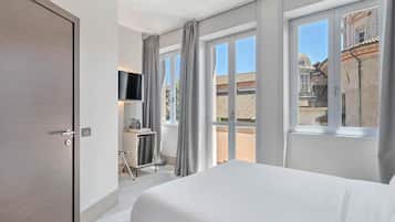 Ein Hotelzimmer mit einem Bett, einem Schreibtisch mit Stuhl, einem an der Wand befestigten Fernseher und großen Fenstern mit Vorhängen.