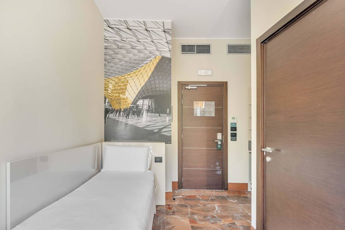 A hotel room with a bed, a door, and a wall-mounted air conditioning unit.