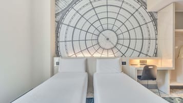 Habitación de hotel con dos camas individuales, un tapiz grande en la pared, un escritorio con silla y una mesita de noche.