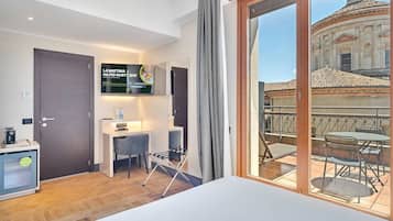 Habitación de hotel con cama, escritorio, silla, televisor y balcón con vista a un edificio.