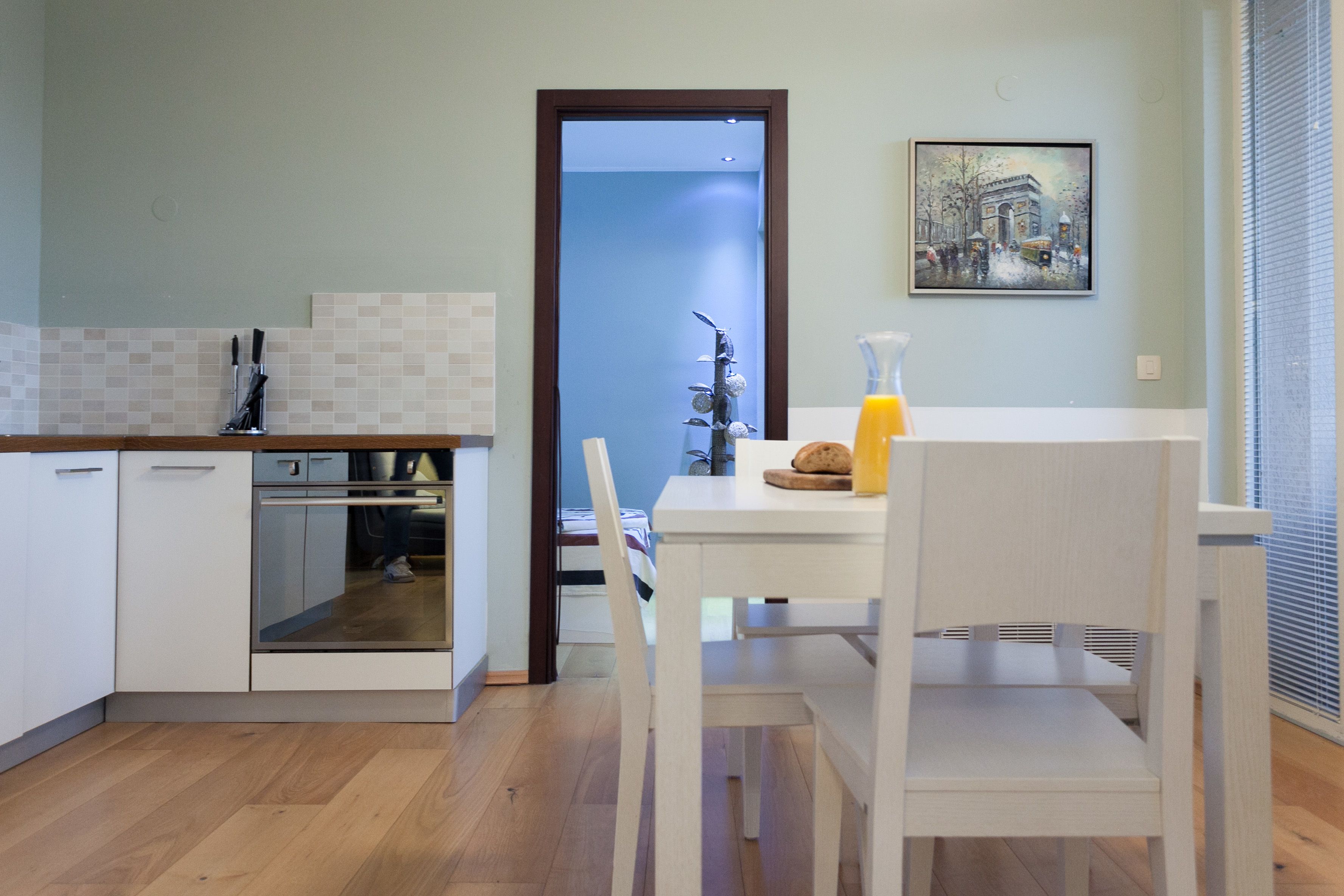 Een moderne keuken met witte kastjes, een inbouwoven en een eethoek met een witte tafel en stoelen.