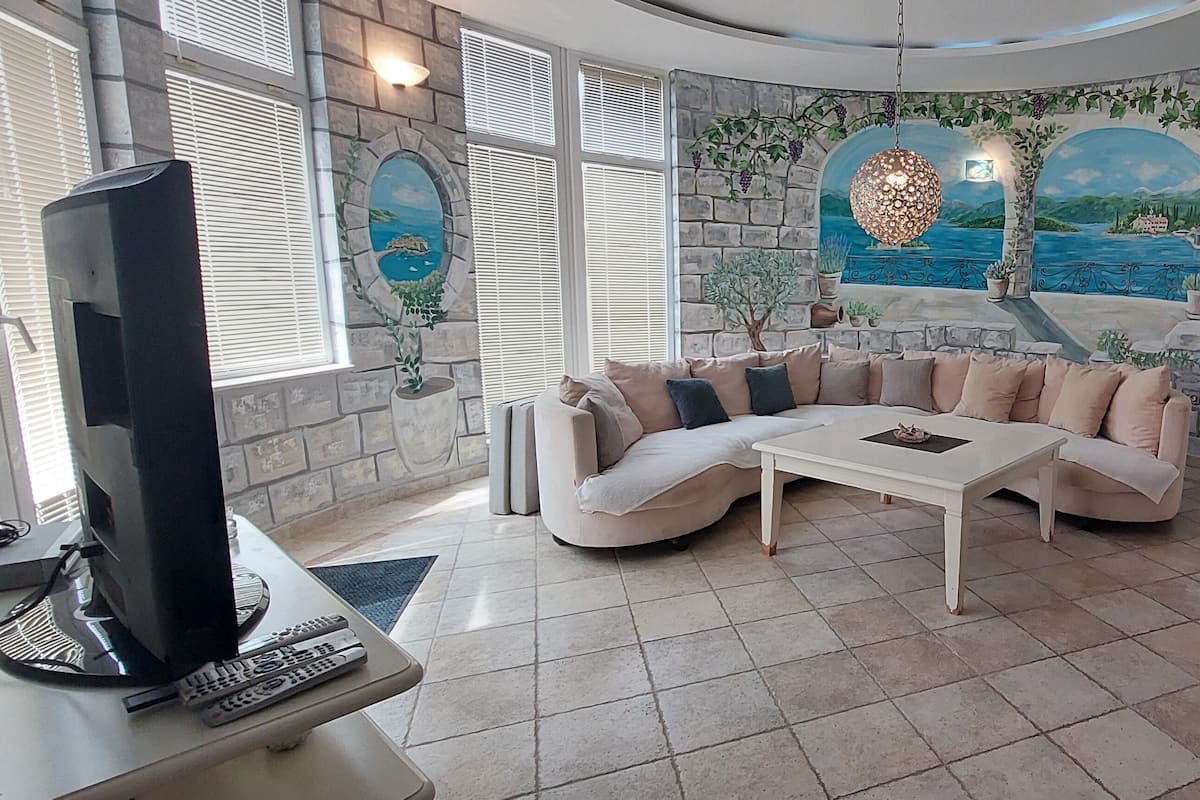 Una sala de estar con una pared curva de piedra, un sofá seccional beige, una mesa de centro y un televisor de pantalla plana sobre un mueble.