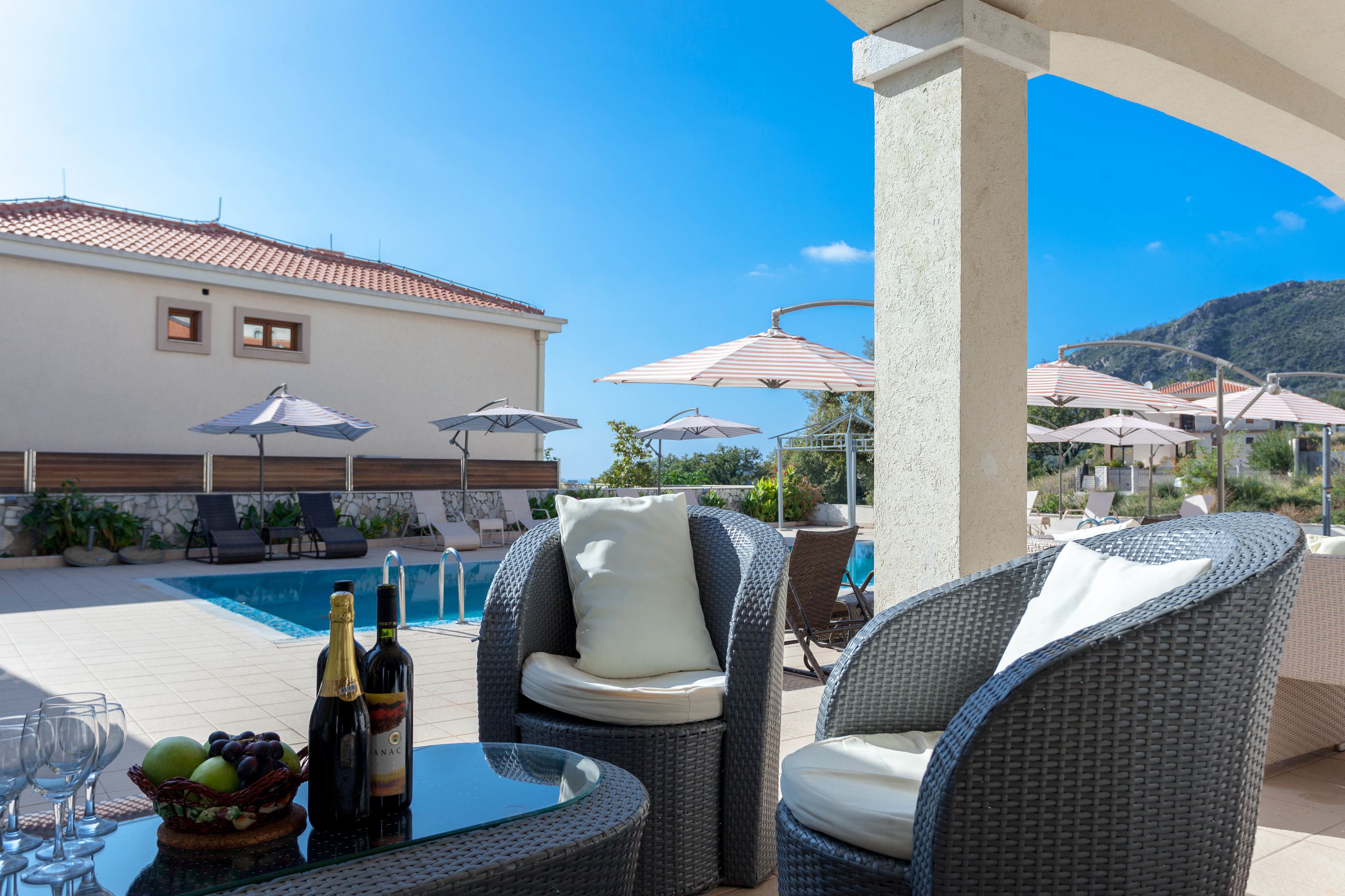 A poolside area with wicker furniture, umbrellas, and a table with bottles and glasses.