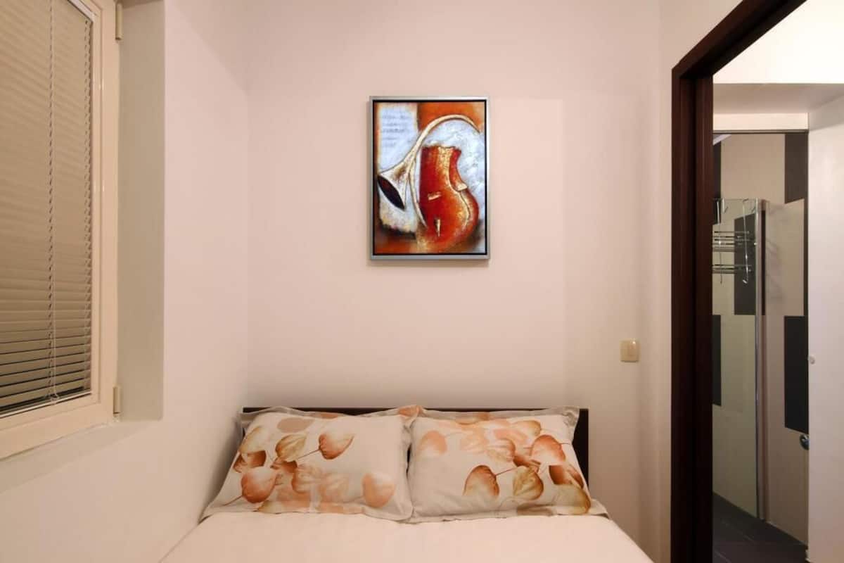 Un dormitorio con cama, un cuadro en la pared y una ventana con persianas.