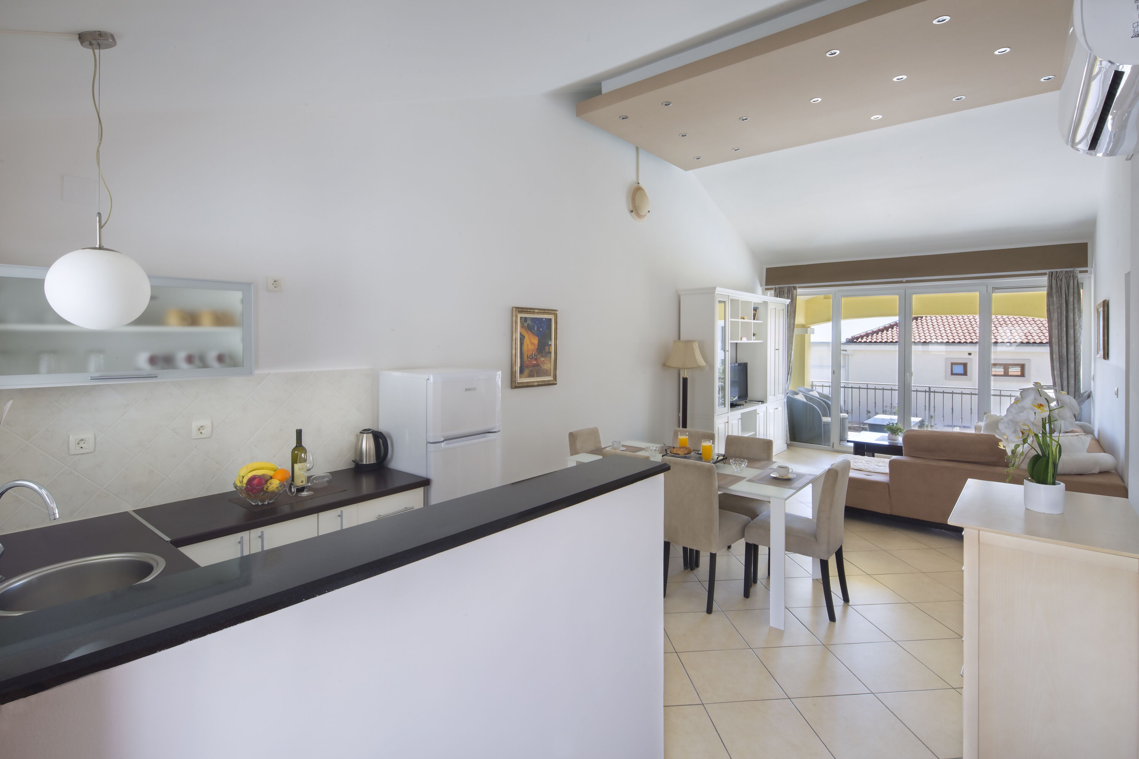 A modern kitchen with a black countertop, white cabinets, and a dining area with a table and chairs.