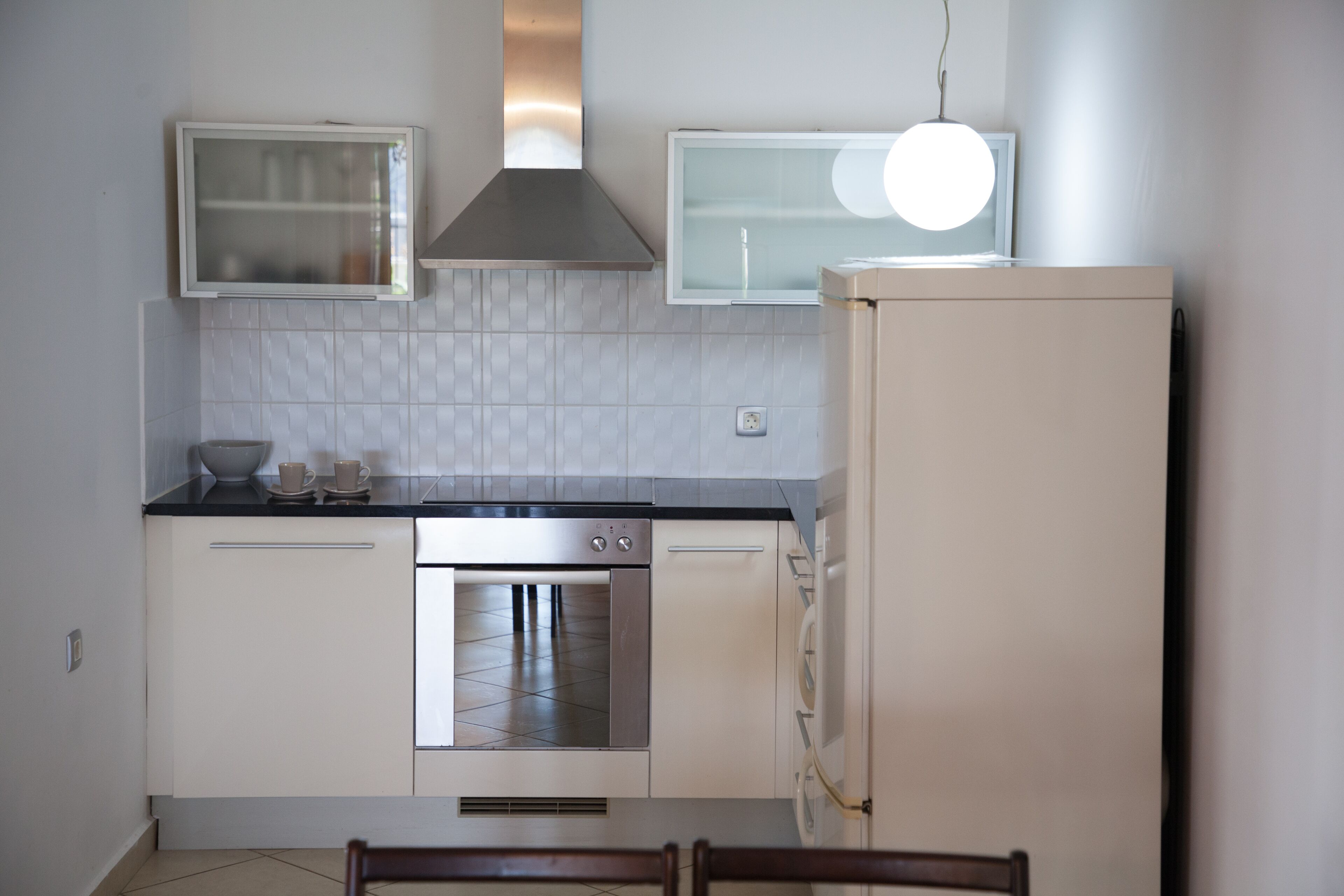 A compact kitchen with white cabinets, a stainless steel oven, a built-in microwave, and a refrigerator.