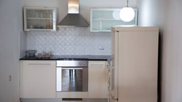 A compact kitchen with white cabinets, a stainless steel oven, a built-in microwave, and a refrigerator.