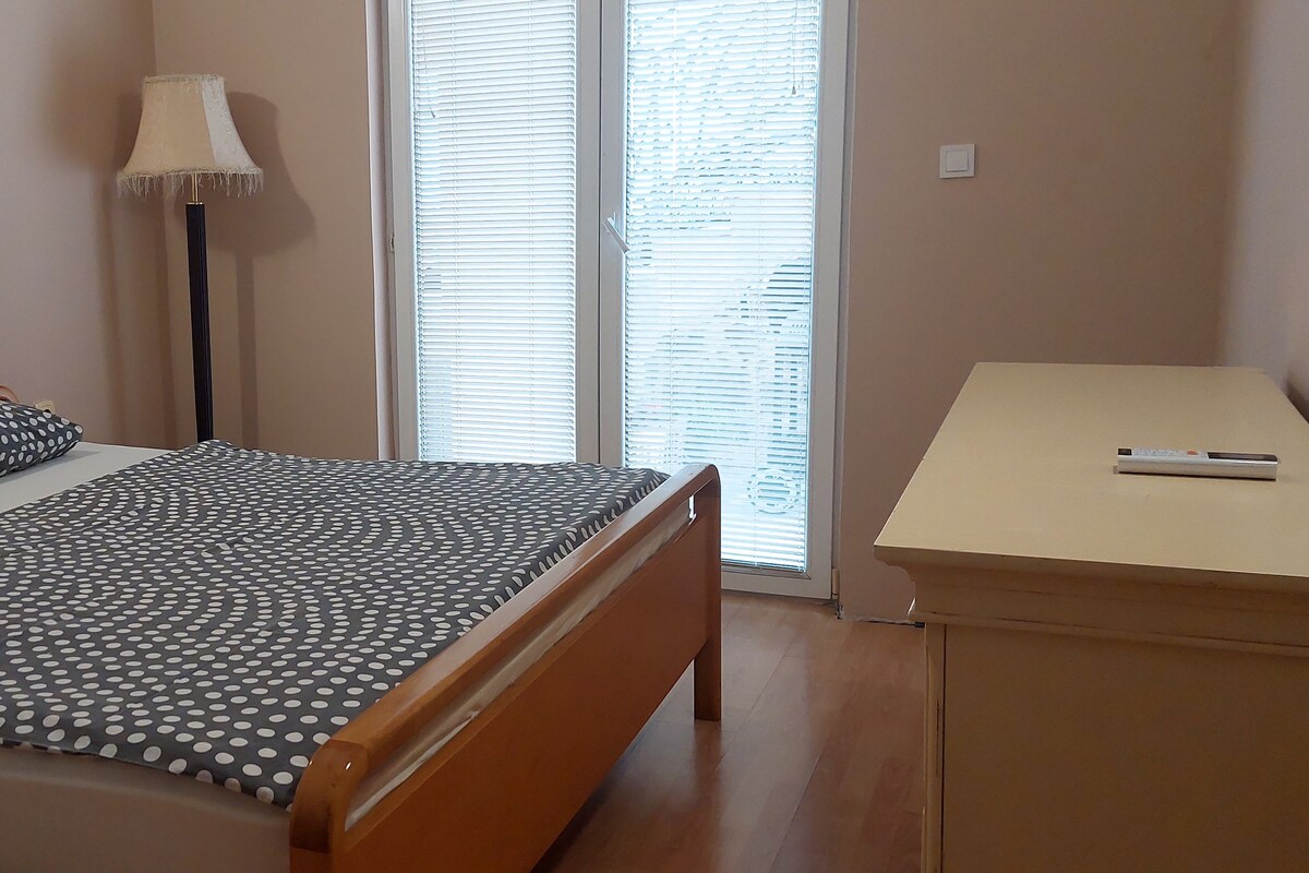 Un dormitorio con cama, dos almohadas, una lámpara de pie, un escritorio y una ventana con persianas.