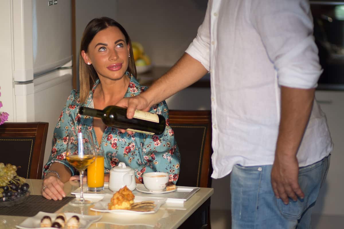 Una mesa de comedor con una botella de vino, un vaso de jugo de naranja y un plato de comida.