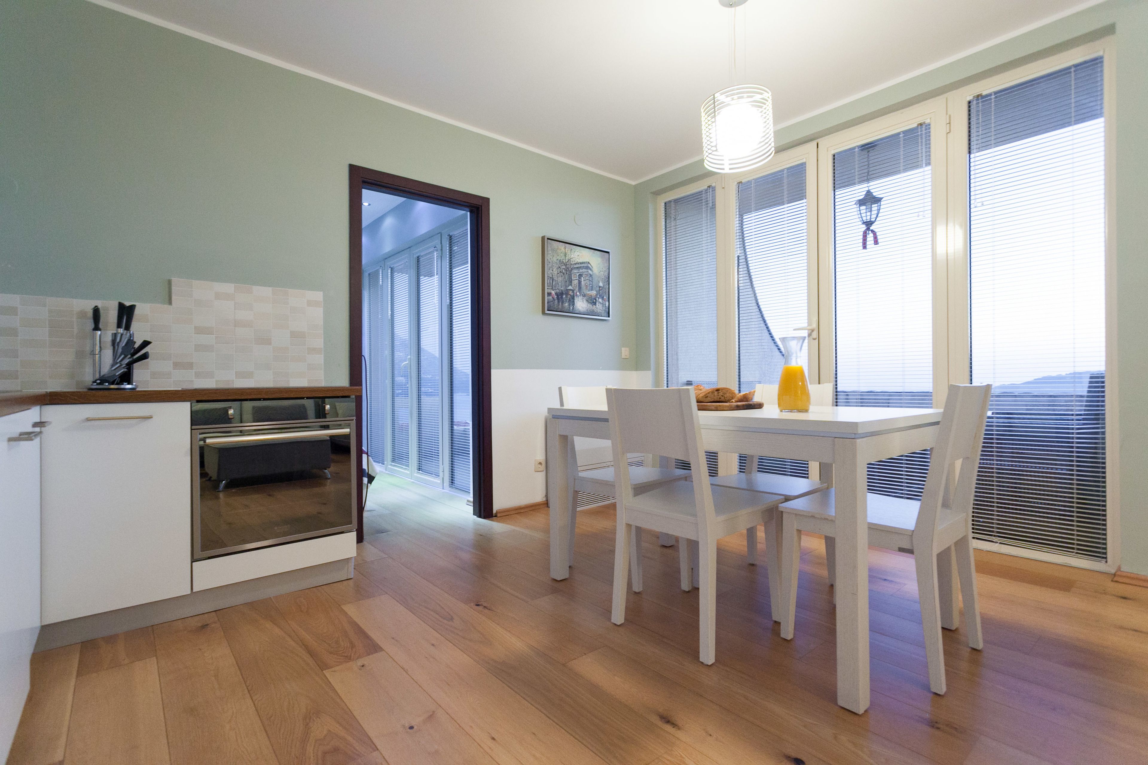 A modern kitchen with white cabinets, a built-in oven, and a dining area with white chairs and a table.