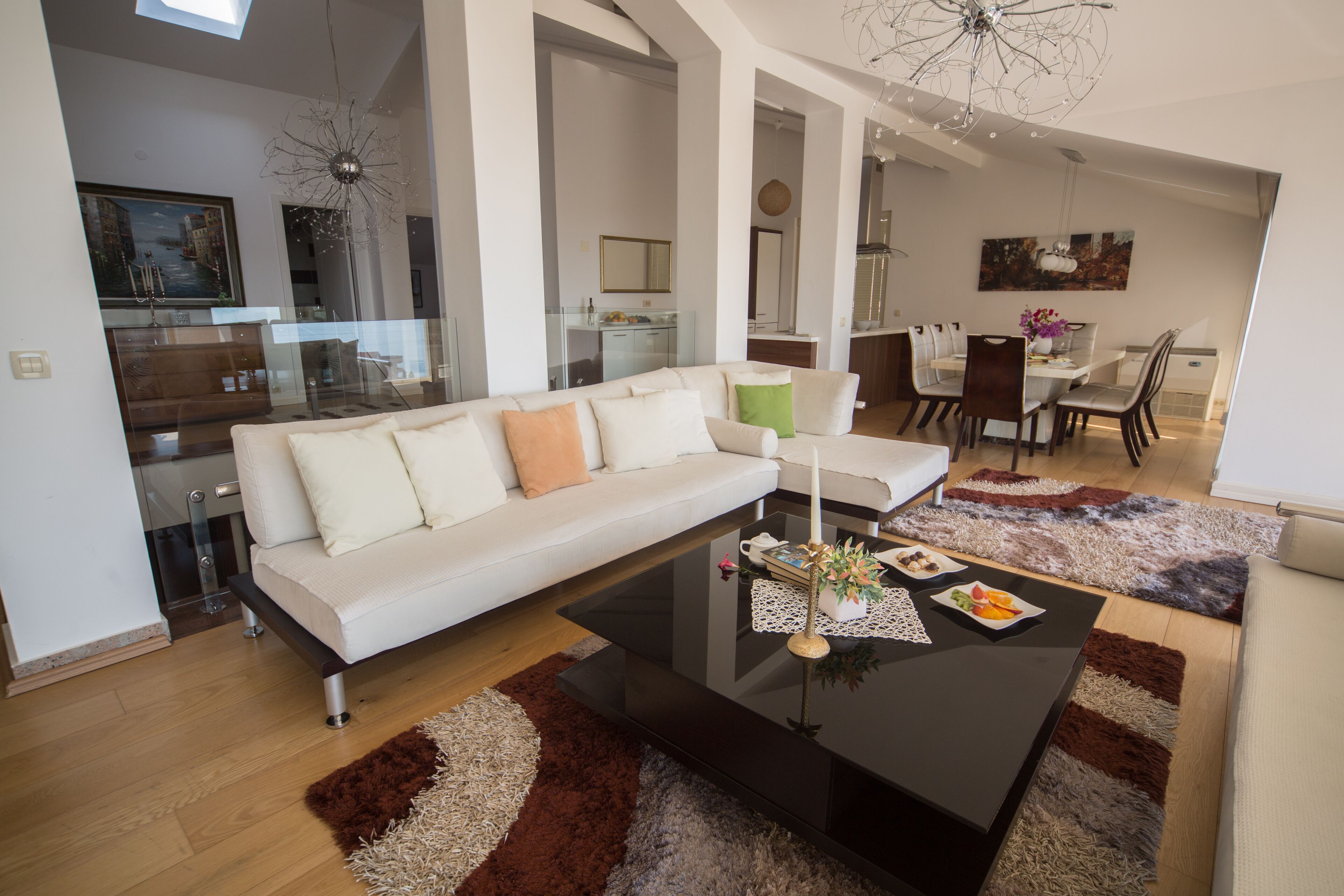 A modern living room with a white sofa, a glass coffee table, and a dining area with a white table and chairs.