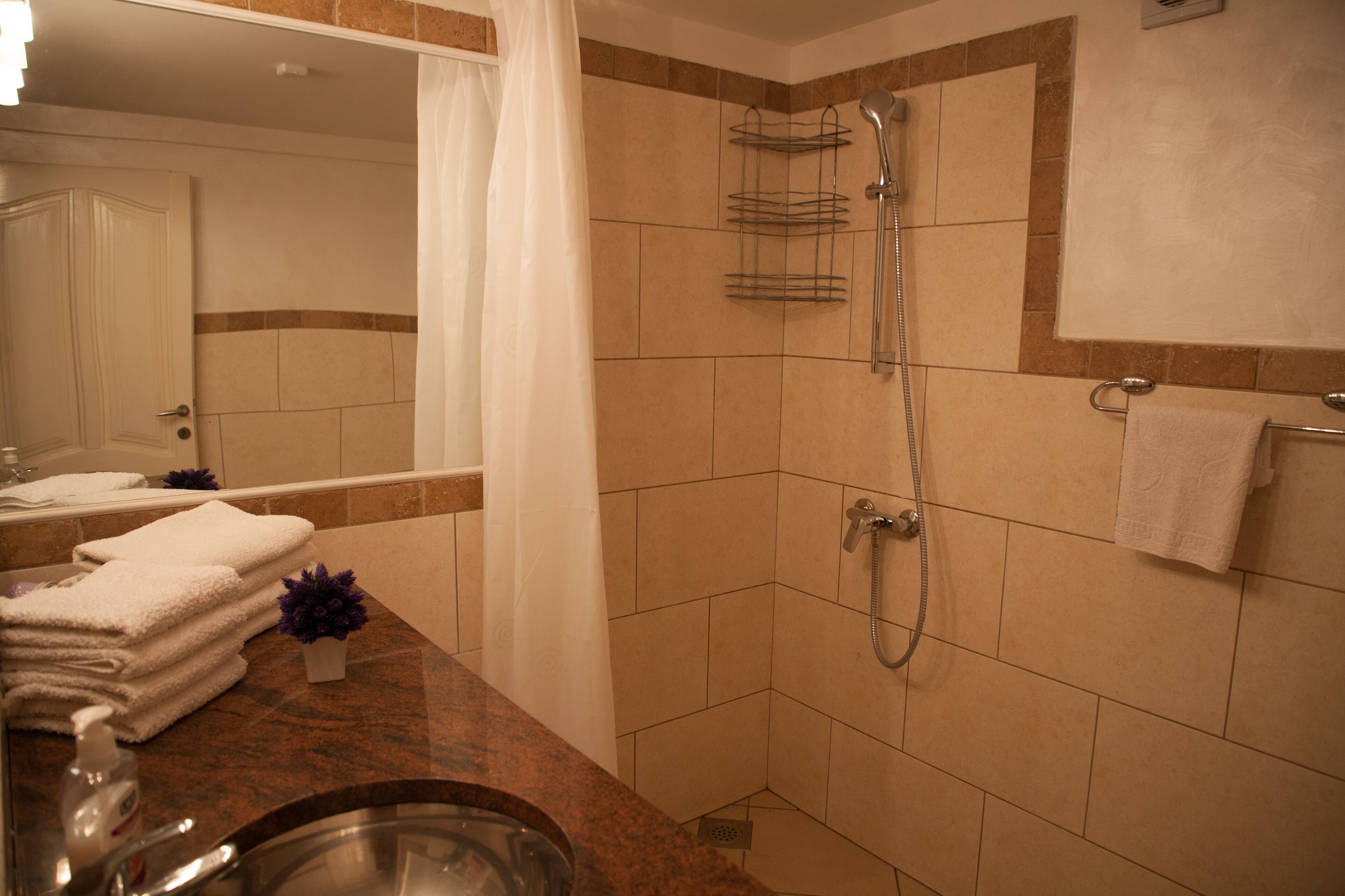 A bathroom with a shower, a sink, and a stack of white towels.