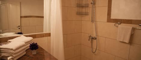 A bathroom with a shower, a sink, and a stack of white towels.