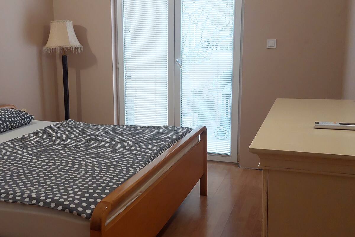 Un dormitorio con cama, dos almohadas, una lámpara de pie, un escritorio y una ventana con persianas.