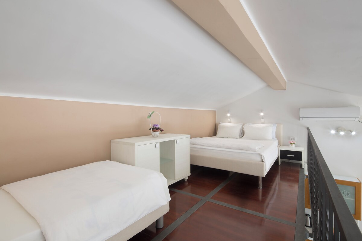 Habitación de hotel moderna con dos camas, un mueble pequeño y un balcón con barandilla.