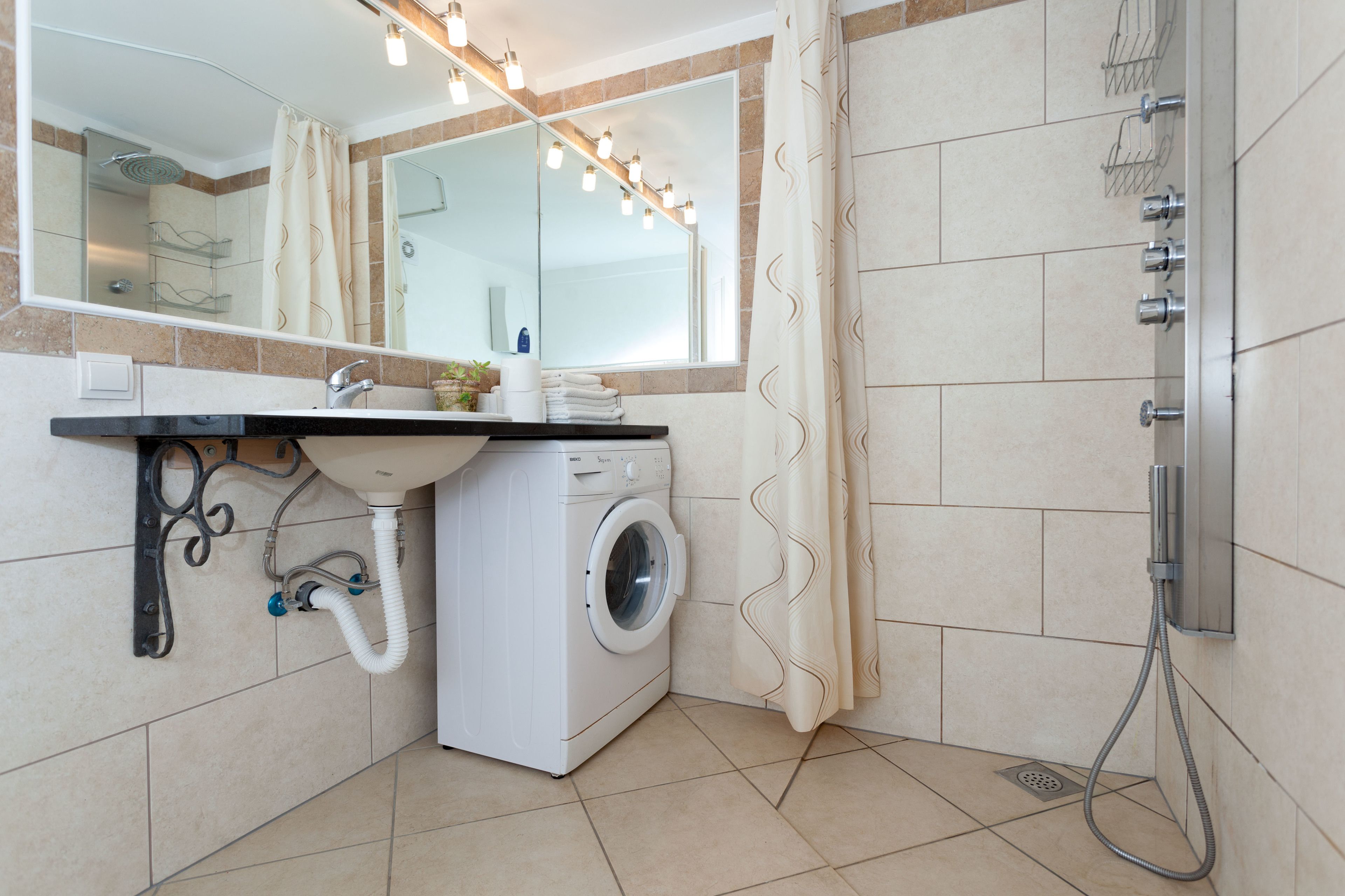 Une salle de bain moderne équipée d’un lavabo, d’un miroir, d’un lave-linge et d’une douche.