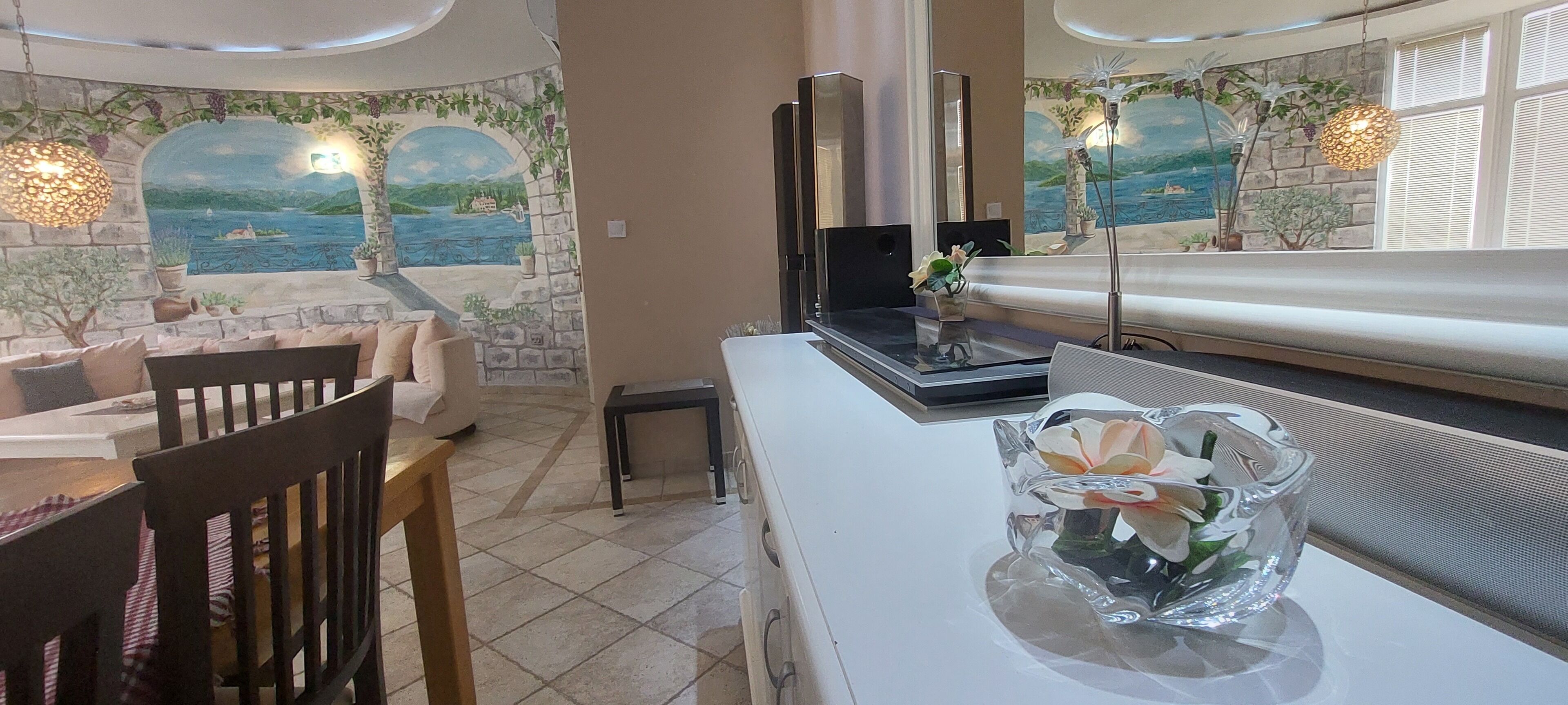 A cozy room with a stone wall mural, a white sofa, a wooden dining table, and a clear glass vase with flowers.