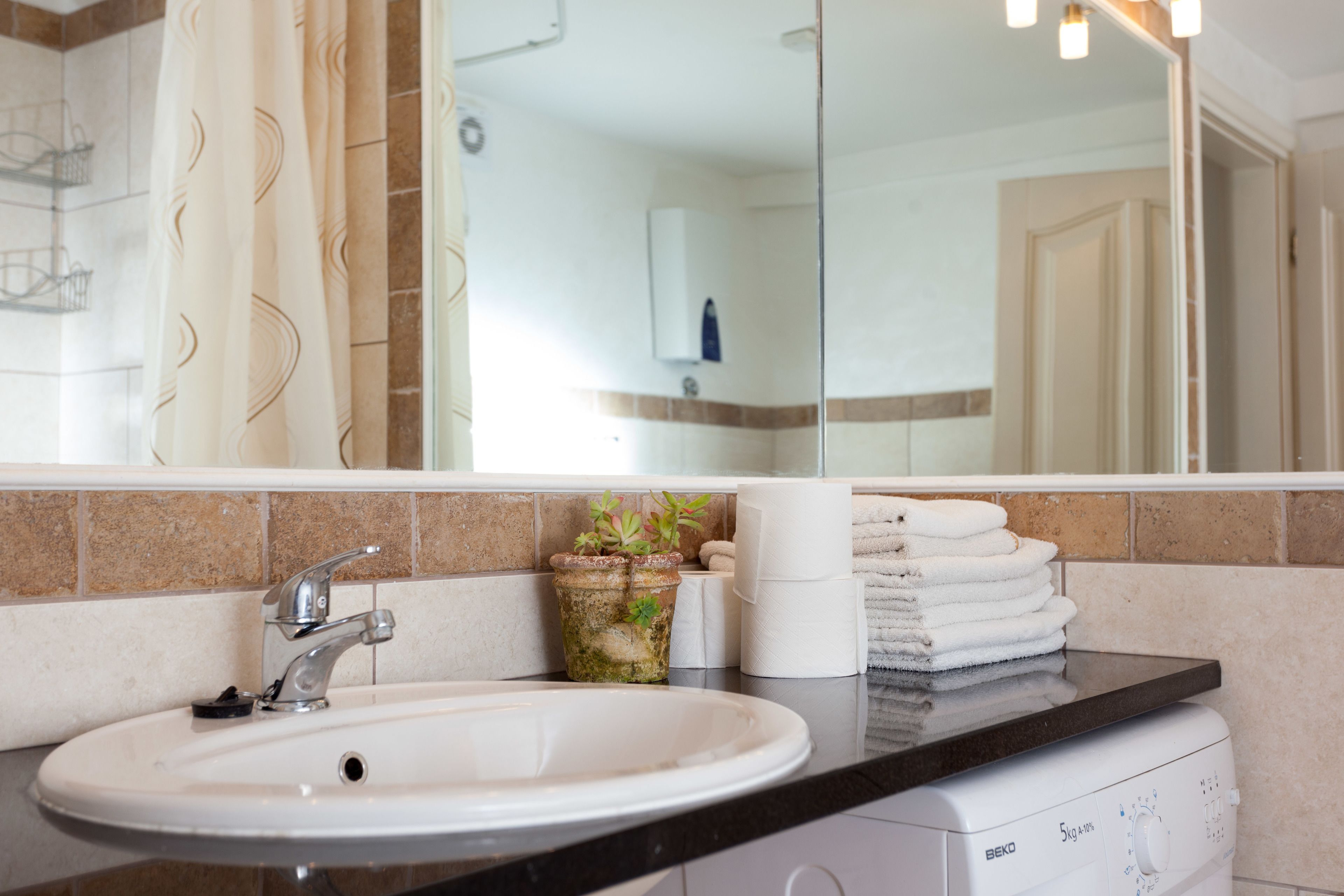 A bathroom with a sink, a mirror, a towel rack, and a washing machine.