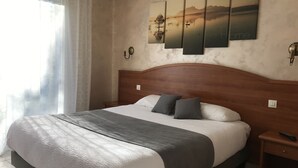 Una cama bien tendida con un edredón gris y blanco, un cabecero de madera y una mesita de noche con un control remoto.