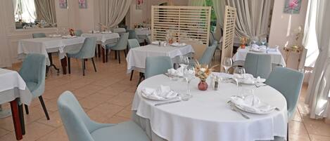 Un comedor con mesas redondas, sillas azul claro y manteles blancos.